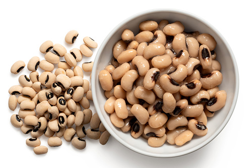 bowl of cooked black eyed peas next to pile of uncooked black eyed peas