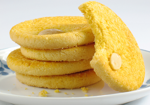 five chinese almond cookies on a white plate, one with a bite out of it