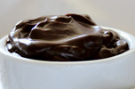 chocolate pudding in a white bowl next to a spoon and napkin