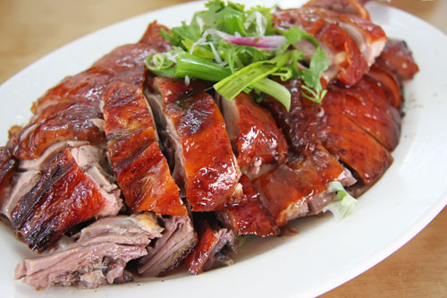 sliced roast duck with fresh herbs on a white plate