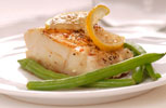 cooked cod fish on a plate with lemon and green beans