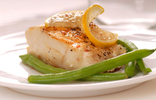 cooked cod fish on a plate with lemon and green beans