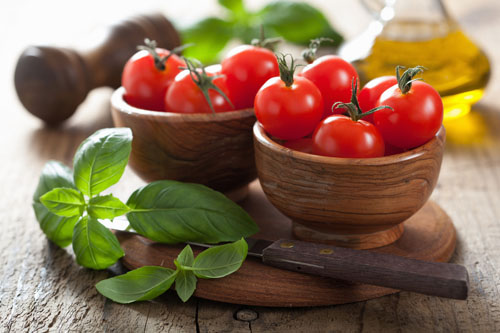 cherry tomatoes with stems in two wooden bowls next to herbs