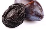 dried prune sitting next to a fresh prune-plum