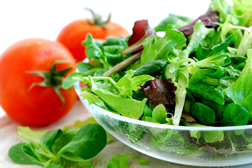 mixed greens in a glass bowl and two whole raw tomatoes