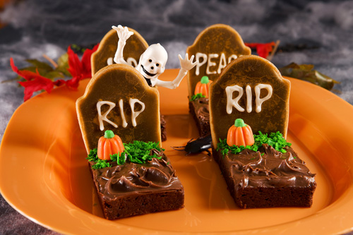 four decorated tombstone brownies on an orange plate