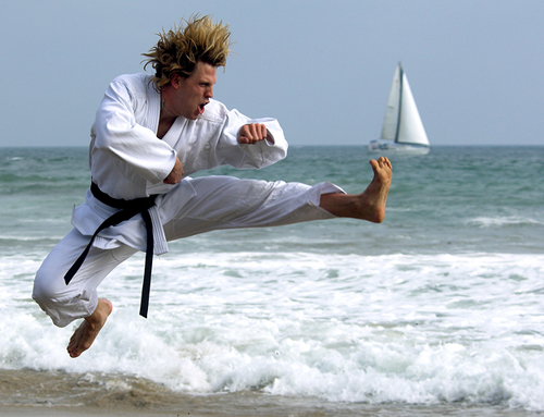 man practicing kung fu on a beach as a sailboat floats by