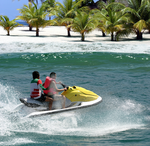 two people riding a jetski off a beach with palm trees